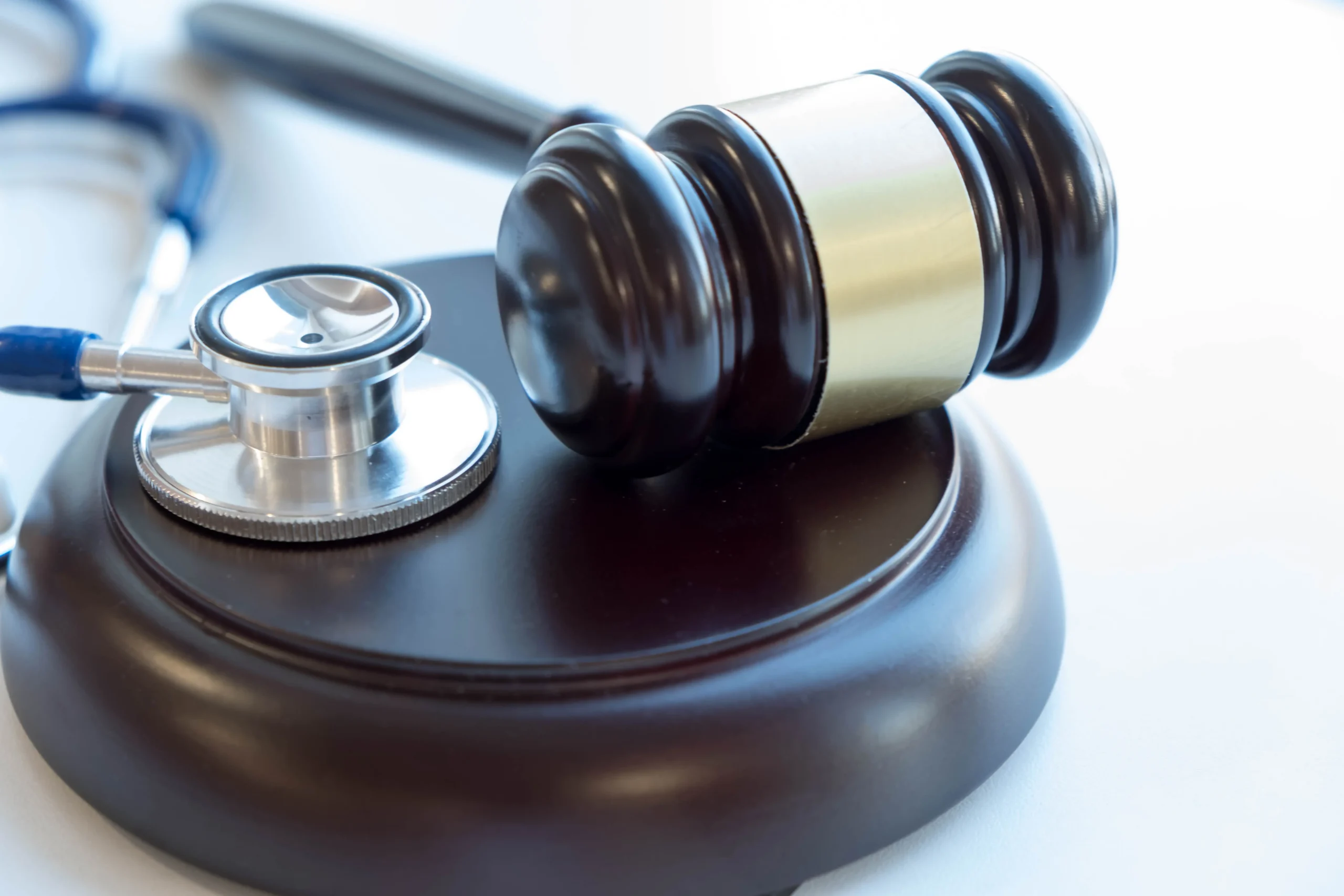 Gavel resting on a wooden base next to a silver stethoscope on a light background.