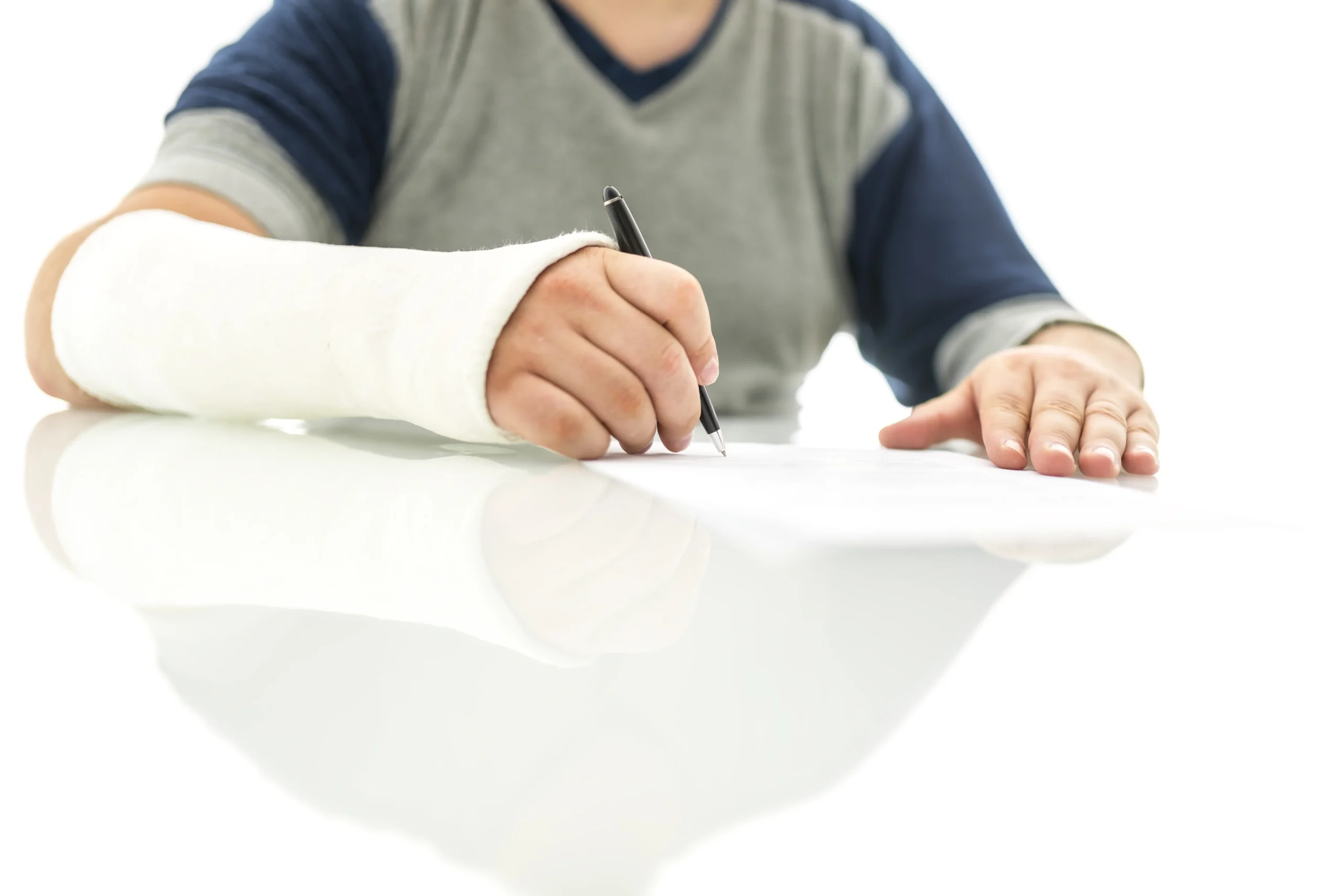Person with a cast on their arm writing on a sheet of paper with a black pen on a reflective surface.