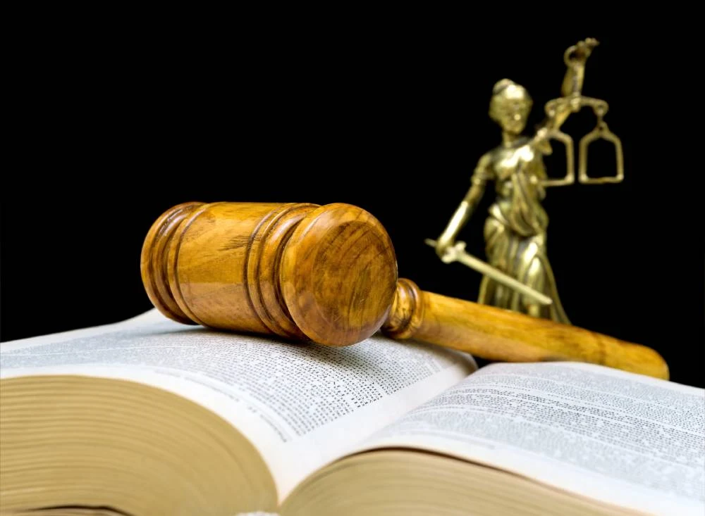 Wooden gavel resting on an open law book, with a golden Lady Justice statue in the background.