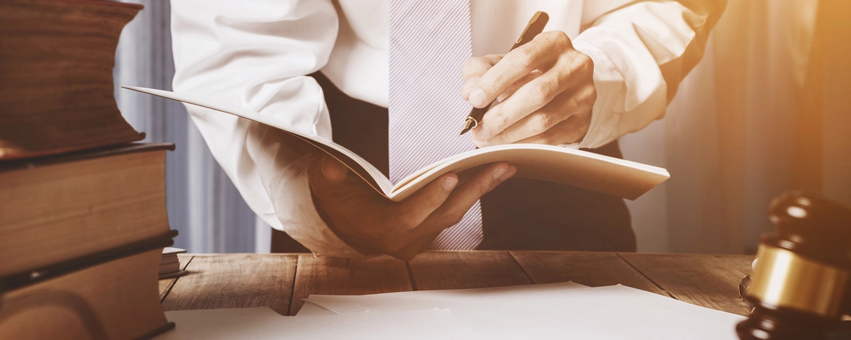 Lawyer writing in a notebook at a desk with legal books and a gavel, illustrating legal fees as part of DUI cost.