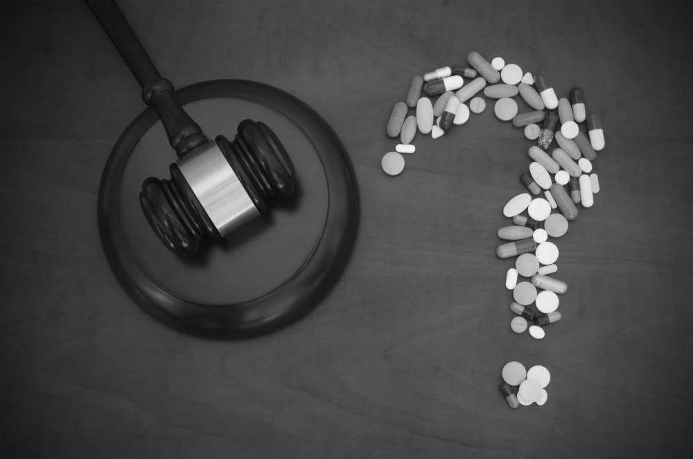 Gavel beside a question mark made of various colored pills on a wooden surface.