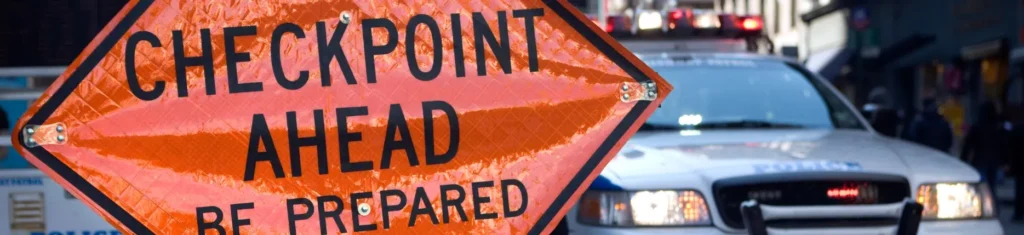DWI checkpoint sign with police car and flashing lights on city street.