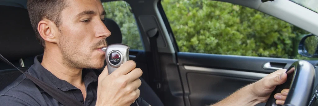 Man blowing into an ignition interlock device while seated in a car, indicating he may have blown a violation on Smart Start.