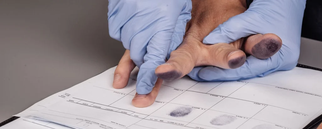 Close-up of gloved hands fingerprinting a suspect on an arrest card, representing the legal process when sexual assault charges are dropped.