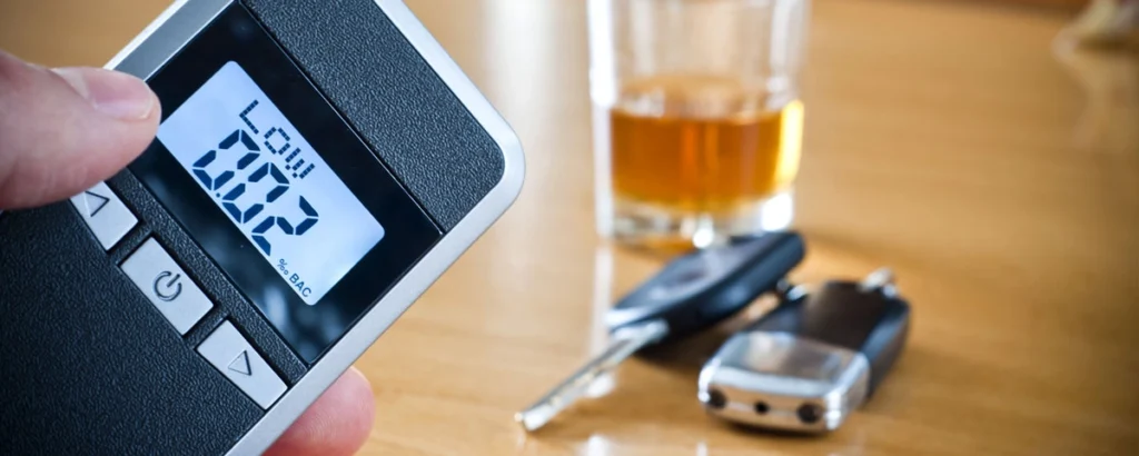 Close-up of a breathalyzer showing a low BAC reading, with car keys and a glass of liquor in the background, symbolizing appreciable impairment.