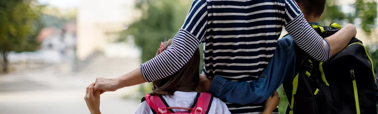 Mother walking two children to school, one with a pink backpack and the other with a black and neon green backpack, representing child custody in NC.