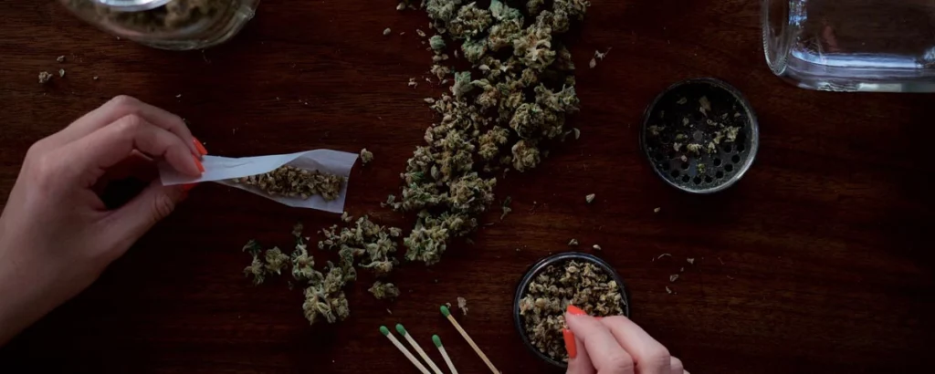 Hands preparing a marijuana joint on a wooden table with loose cannabis and a grinder, representing drug offenses affected by federal sentencing guidelines.