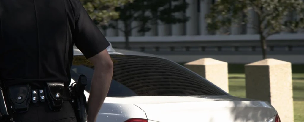 Police officer standing beside a white car during a stop, possibly preparing for a police pat down.