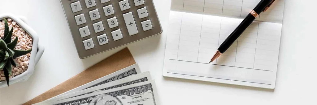 Close-up of a calculator, cash, a pen, and a checkbook representing attorney's fees in civil cases.