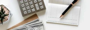 Close-up of a calculator, cash, a pen, and a checkbook representing attorney's fees in civil cases.