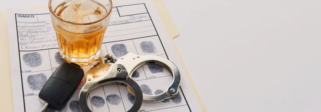 Glass of liquor, car key, and handcuffs on a fingerprint record sheet, symbolizing legal consequences tied to DWI sentencing.
