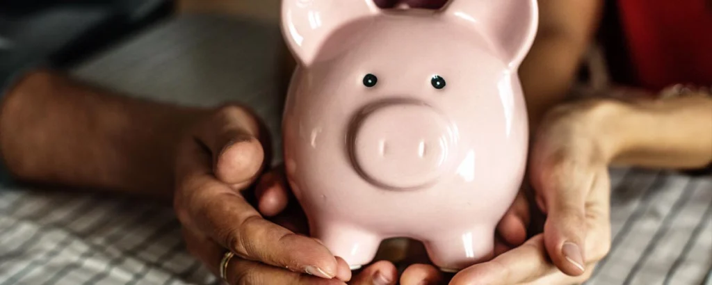 Close-up of a couple’s hands holding a pink piggy bank together, symbolizing financial decisions involving child support deviation.