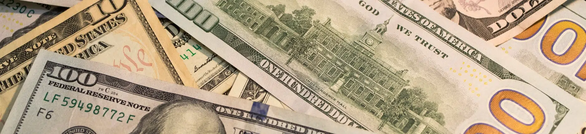 A close-up image of various U.S. dollar bills, including $100, $20, and $10 notes, illustrating financial considerations related to child support imputed income.