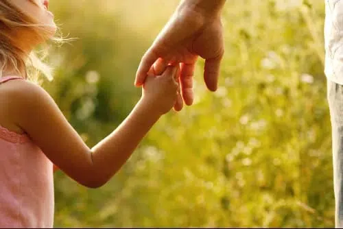 Parent holding a young child’s hand in a sunny field.