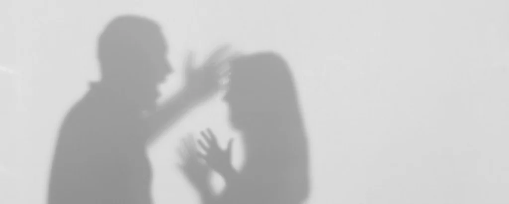Shadow of a man raising his hand toward a woman who appears frightened, symbolizing allegations and the complexity of false assault charges.