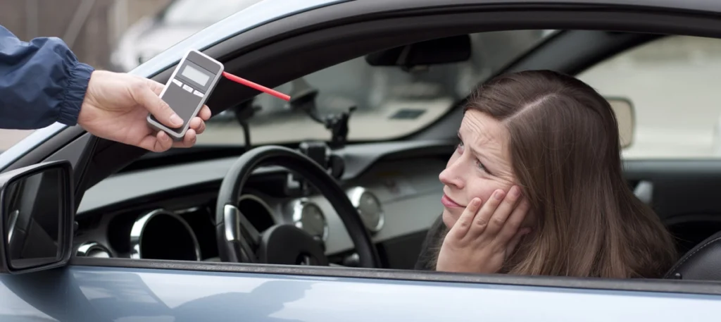Woman in a car looking concerned as a police officer holds a breathalyzer through the window, illustrating issues related to license after a DUI.