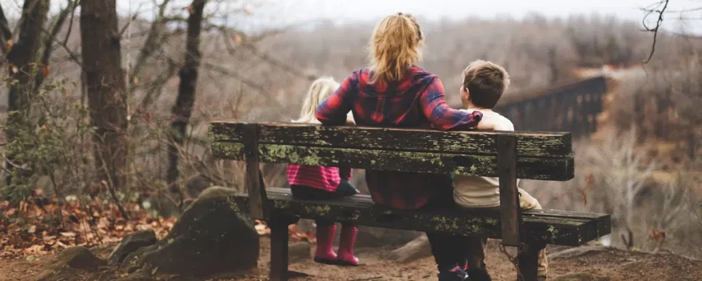 Parent sitting on a bench with two children overlooking a forest, symbolizing a child custody trial.