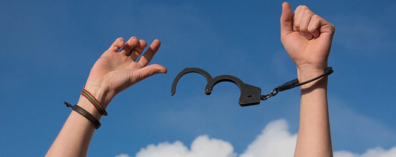 Hands raised toward the sky with one handcuff open and dangling, symbolizing sentencing relief under the NC First Step Act.