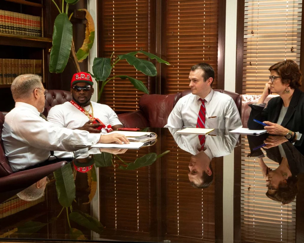 Client Michael Terry in a white shirt and red hat meeting with attorneys at a law office, related to the Yo Gotti lawsuit.