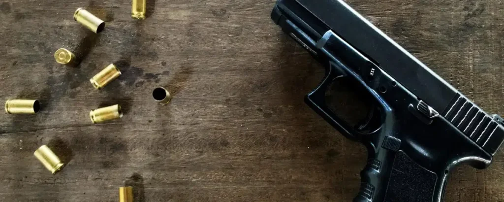 Handgun with spent shell casings on a wooden table, symbolizing legal issues involving bringing a firearm onto courthouse property.