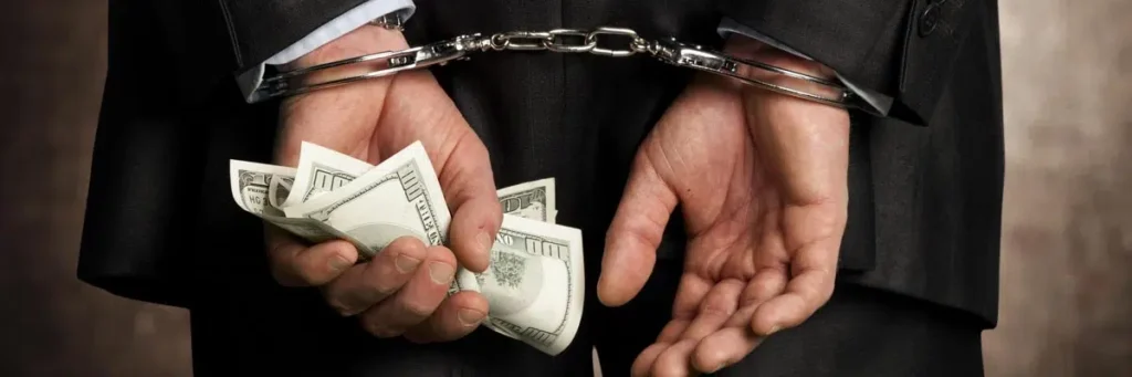 Man in a suit handcuffed behind his back holding cash, representing arrest for obtaining property by false pretenses.