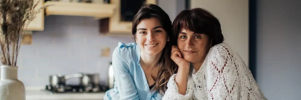 Mother and teenage daughter smiling together in a kitchen after receiving an emergency custody order.