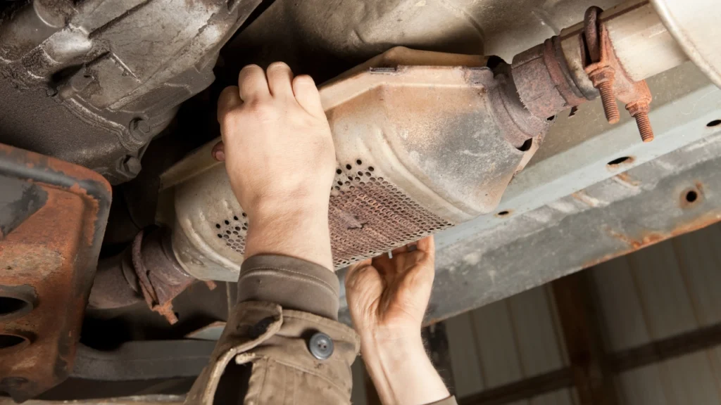 Mechanic working on a catalytic converter beneath a vehicle.