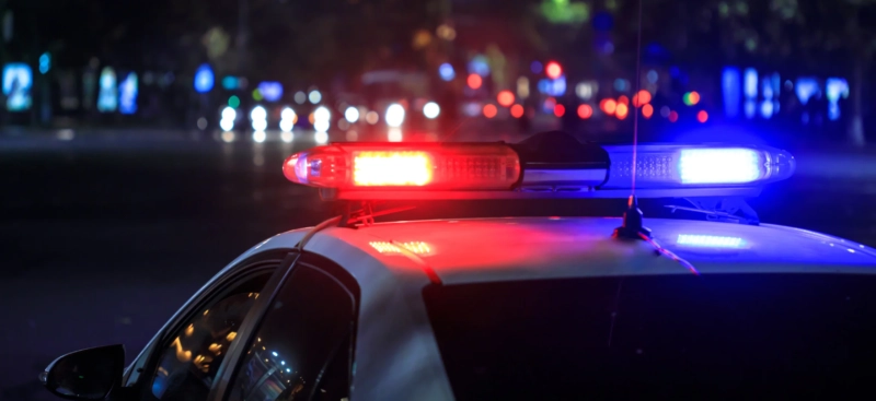 Police car with flashing red and blue lights at night on a city street.