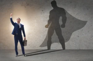 Man in a business suit with raised fist casts superhero shadow on wall.