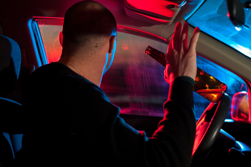 Man drinking beer in car with police lights at night.