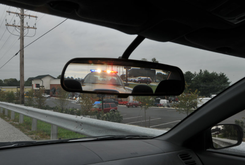 Rearview mirror reflection of police car with flashing red and blue lights.