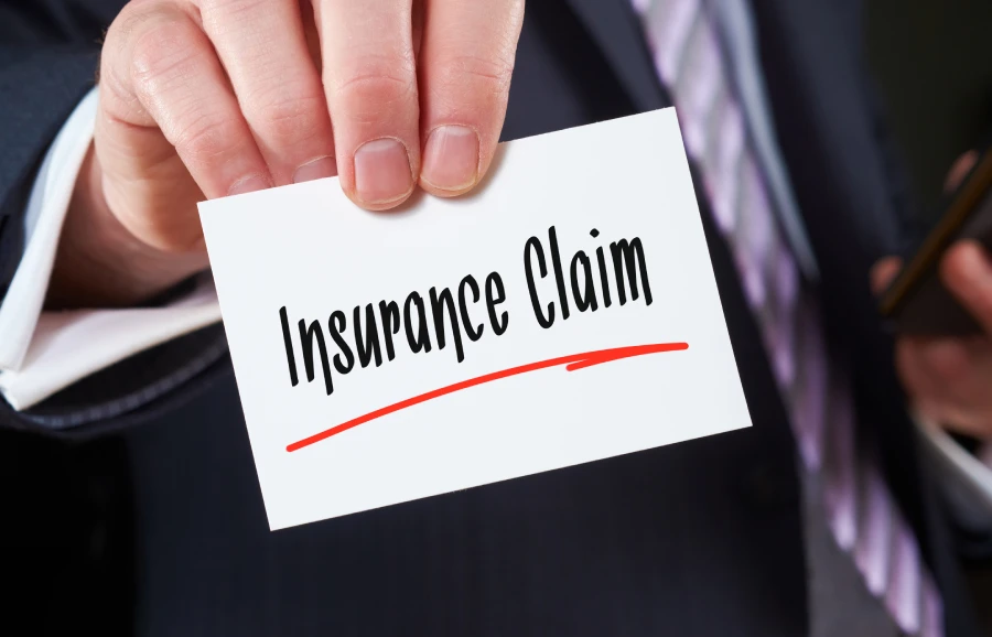 Hand holding a card that says "Insurance Claim" in bold black letters with a red underline.