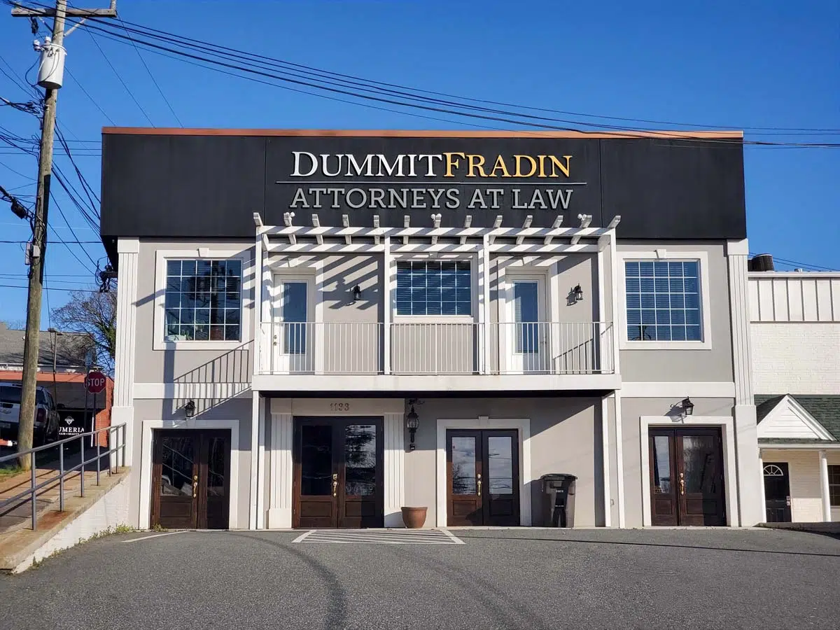 McMinn, Fradin, Gray & Logan Attorneys at Law building with a black sign, white facade, and two sets of wooden doors. Clear blue sky.