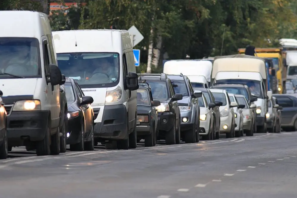 Traffic jam with various cars and vans on a city street, surrounded by greenery and road signs.