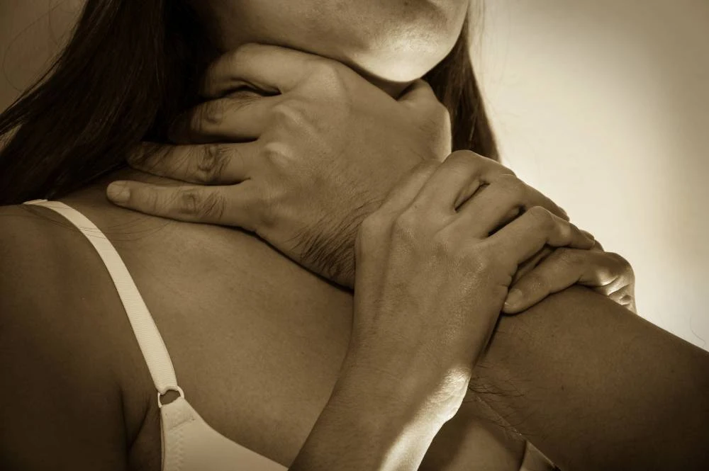 Hands gripping a woman's neck in a sepia-toned image, conveying a sense of tension and distress.