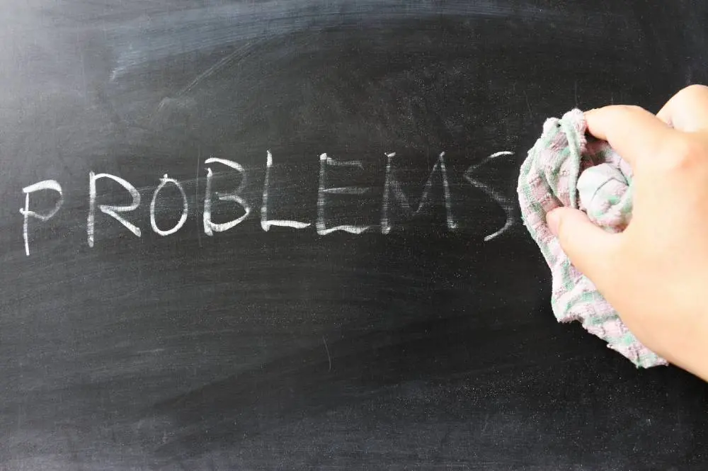 Hand wiping the word "PROBLEMS" off a black chalkboard with a checkered cloth.