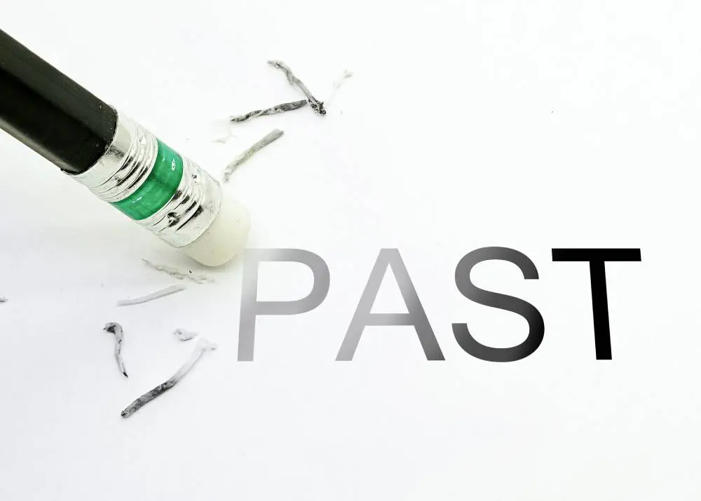 Eraser partially removing the word "PAST" on white paper, with shavings scattered around.