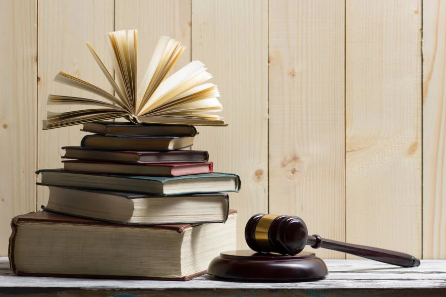 Stack of books with an open book on top and a wooden gavel beside it, set against a wooden background.