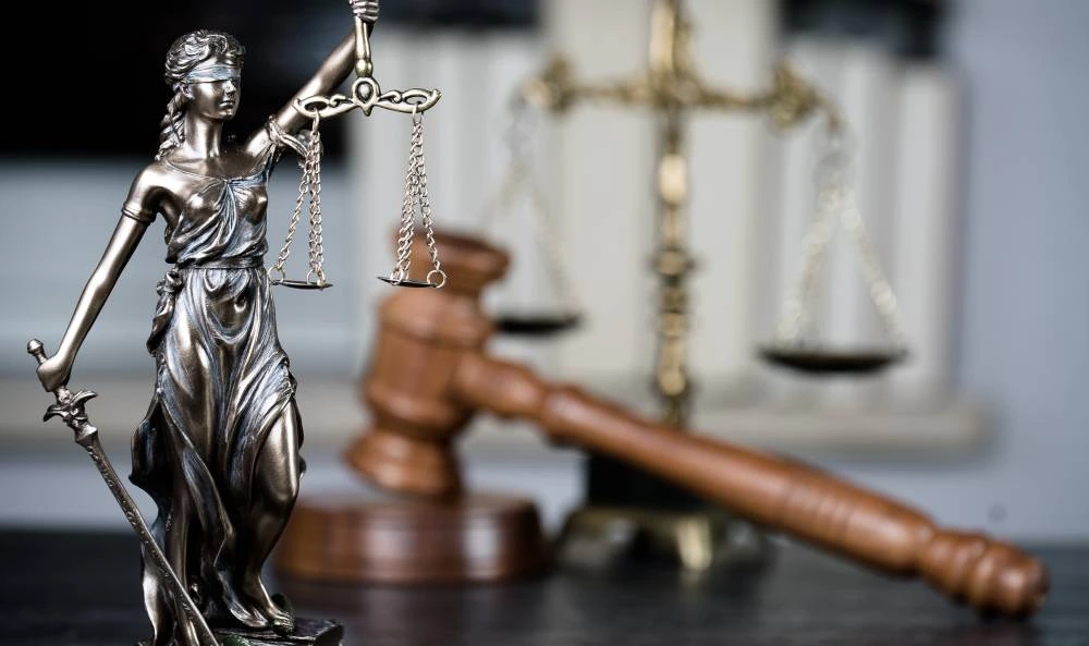Bronze Lady Justice statue holding scales and sword, with a wooden gavel and scales in the background.