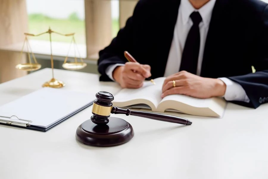 A lawyer in a suit writes notes in a book, with a gavel and scales of justice on the table.