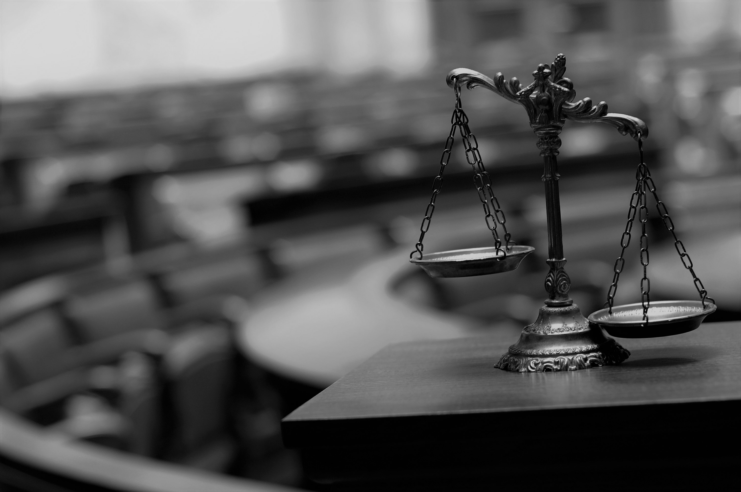 Bronze scales of justice on a wooden table in a blurred courtroom setting.