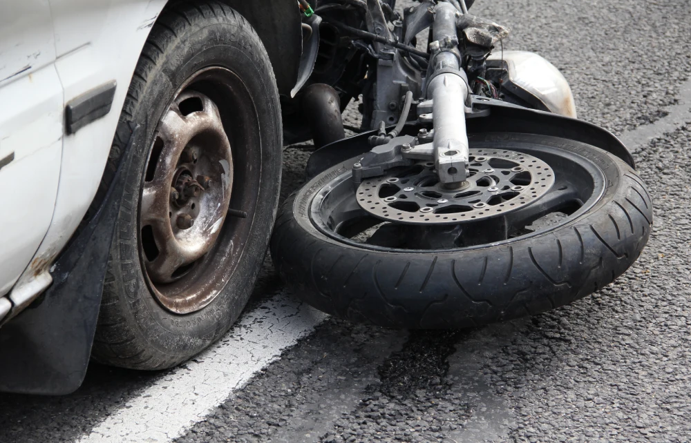 A damaged motorcycle tire rests against a car tire on a cracked asphalt road.