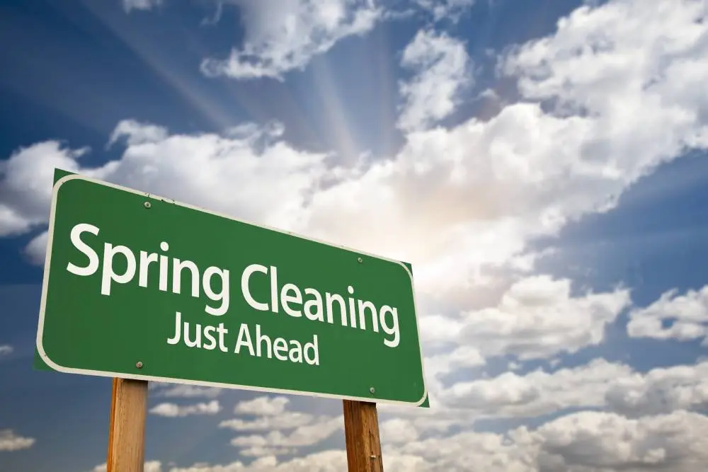 Green road sign reading "Spring Cleaning Just Ahead" against a bright sky with clouds.