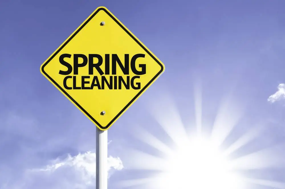 Yellow diamond-shaped sign with "SPRING CLEANING" in bold black letters against a blue sky and bright sun.